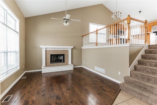 unfurnished living room featuring a tile fireplace, ceiling fan with notable chandelier, hardwood / wood-style flooring, and a wealth of natural light