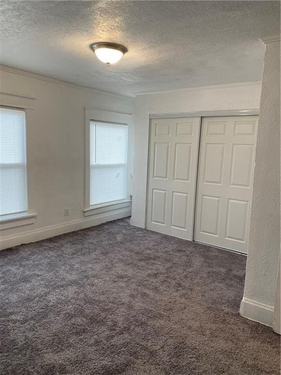 unfurnished bedroom with crown molding, a closet, dark carpet, and a textured ceiling