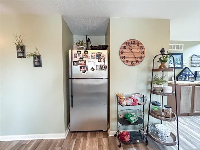 kitchen with hardwood / wood-style floors, a textured ceiling, and stainless steel refrigerator