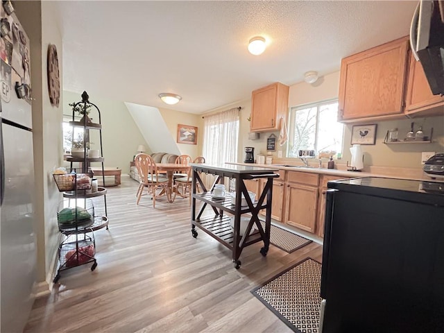 kitchen featuring stove, a textured ceiling, light brown cabinetry, and light hardwood / wood-style flooring