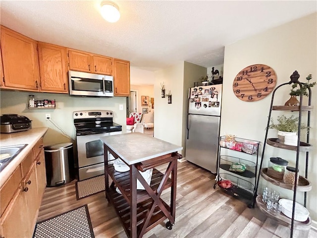 kitchen featuring stainless steel appliances, a textured ceiling, and light wood-type flooring