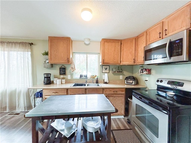 kitchen with sink, stainless steel appliances, hardwood / wood-style floors, and a textured ceiling