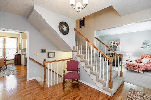 stairs with hardwood / wood-style flooring, a textured ceiling, and a notable chandelier