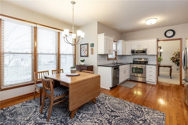 kitchen featuring stainless steel appliances, hanging light fixtures, sink, and white cabinets