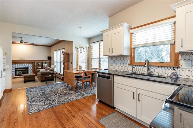 kitchen featuring sink, dishwasher, white cabinets, a tiled fireplace, and decorative light fixtures