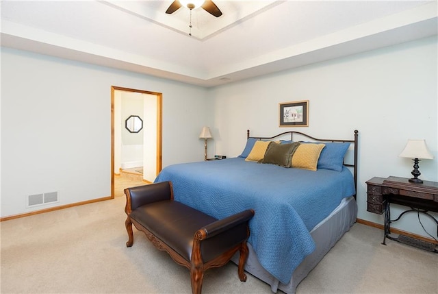 carpeted bedroom featuring ceiling fan, ensuite bath, and a tray ceiling