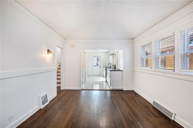 unfurnished living room featuring sink, dark hardwood / wood-style flooring, ornamental molding, and a healthy amount of sunlight