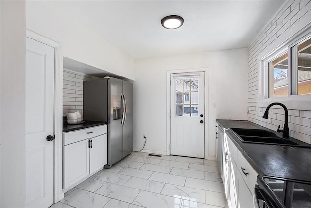 kitchen featuring range, stainless steel fridge with ice dispenser, backsplash, white cabinetry, and sink