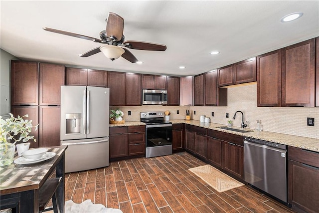 kitchen with appliances with stainless steel finishes, ceiling fan, light stone counters, dark brown cabinetry, and sink