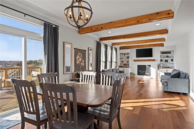 dining space with wood-type flooring, beamed ceiling, built in features, a notable chandelier, and a brick fireplace