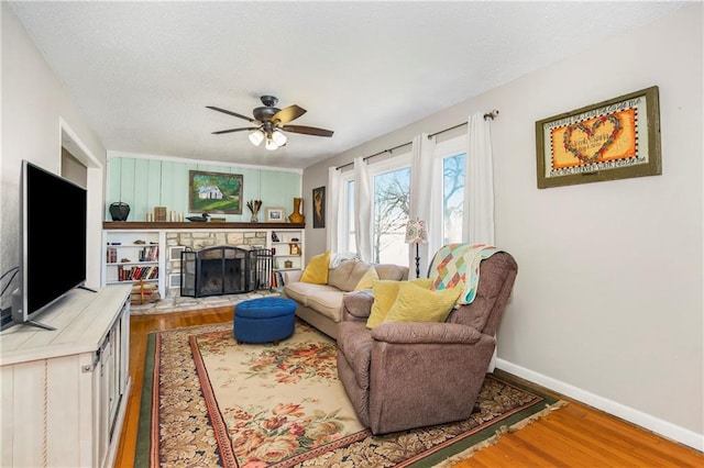 living room with ceiling fan, a stone fireplace, and wood-type flooring