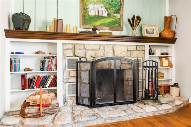 details featuring wood-type flooring, built in shelves, and a stone fireplace