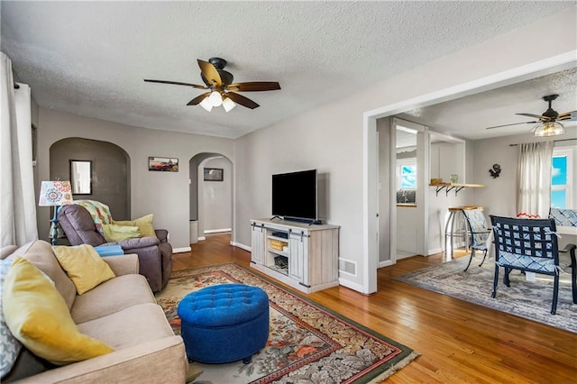 living room featuring ceiling fan, wood-type flooring, a textured ceiling, and a healthy amount of sunlight