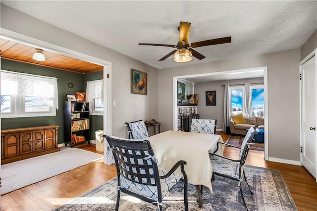 dining space with ceiling fan, hardwood / wood-style floors, a textured ceiling, and a fireplace