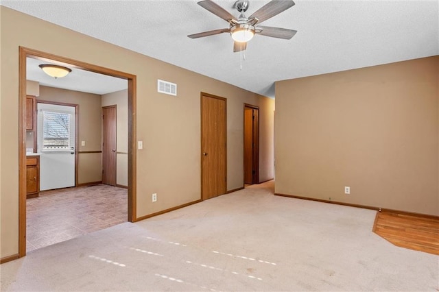 unfurnished bedroom with light colored carpet, two closets, and ceiling fan