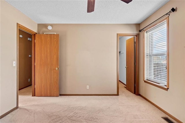 unfurnished bedroom with a walk in closet, a textured ceiling, ceiling fan, and light colored carpet