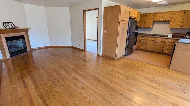 kitchen featuring a tiled fireplace, light hardwood / wood-style flooring, black appliances, and sink