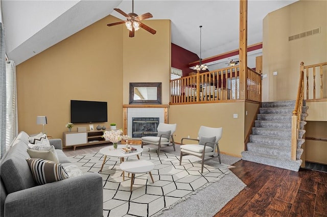 living room featuring hardwood / wood-style flooring, a tiled fireplace, high vaulted ceiling, and ceiling fan