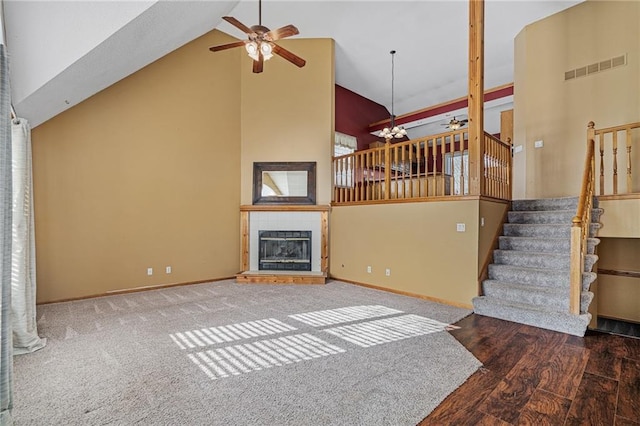 living room featuring dark wood-type flooring, a fireplace, ceiling fan with notable chandelier, and high vaulted ceiling