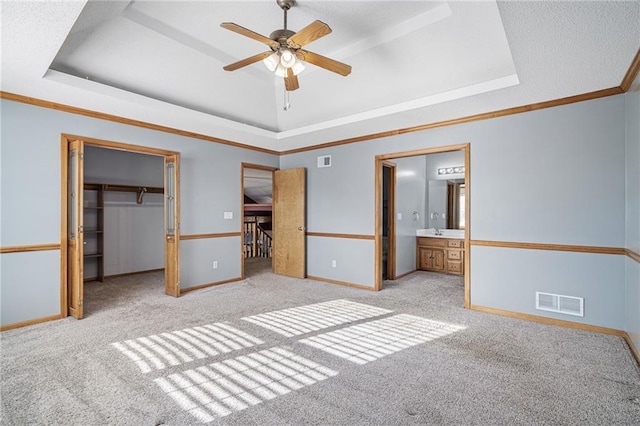 unfurnished bedroom featuring a walk in closet, a tray ceiling, and ensuite bath