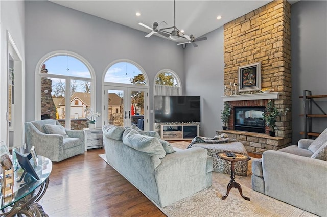 living room featuring ceiling fan, a towering ceiling, a fireplace, and dark wood-type flooring