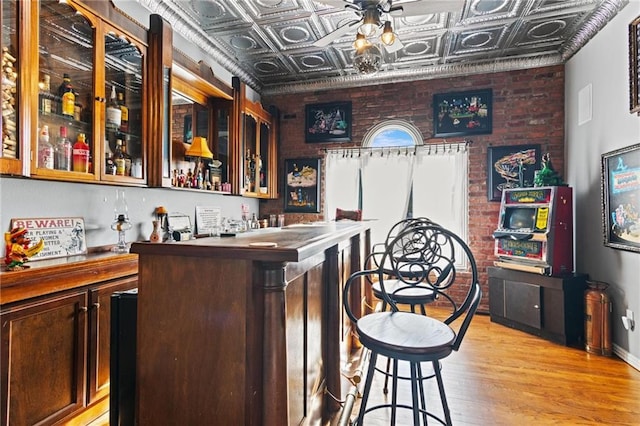 bar with light hardwood / wood-style flooring, brick wall, and dark brown cabinets