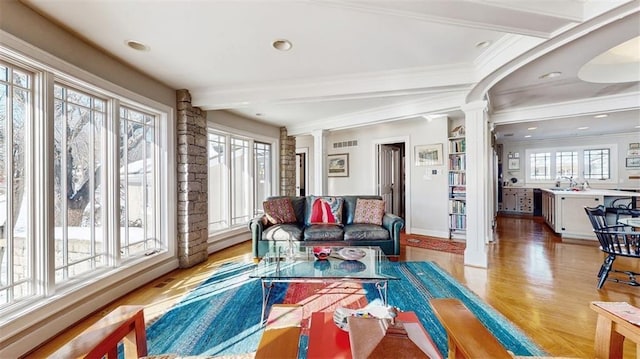 living room featuring decorative columns, beam ceiling, a healthy amount of sunlight, and sink