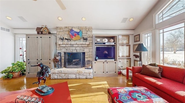 living room with lofted ceiling, ceiling fan, light hardwood / wood-style floors, and a stone fireplace