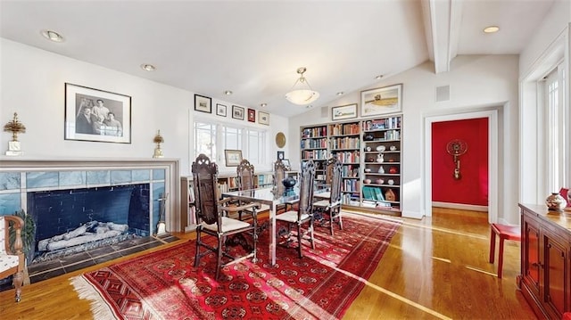 dining space with a tile fireplace, lofted ceiling with beams, and hardwood / wood-style flooring