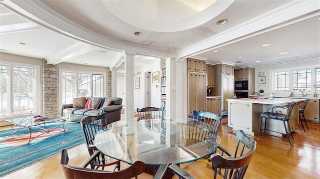 dining area with decorative columns, light hardwood / wood-style floors, crown molding, and a healthy amount of sunlight