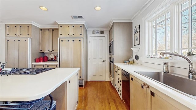 kitchen with black appliances, ornamental molding, light brown cabinetry, sink, and light hardwood / wood-style flooring