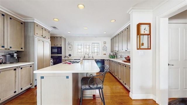 kitchen with hardwood / wood-style flooring, black appliances, decorative backsplash, a kitchen island, and a breakfast bar area