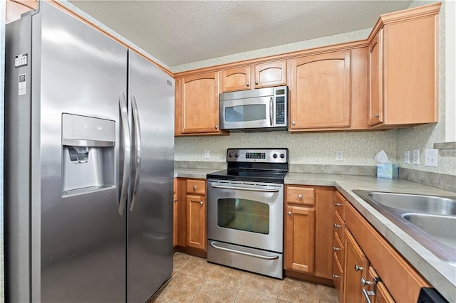 kitchen with appliances with stainless steel finishes, a textured ceiling, light tile patterned floors, and sink