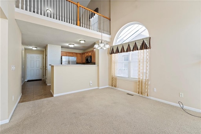 unfurnished living room with light colored carpet, a high ceiling, and a chandelier