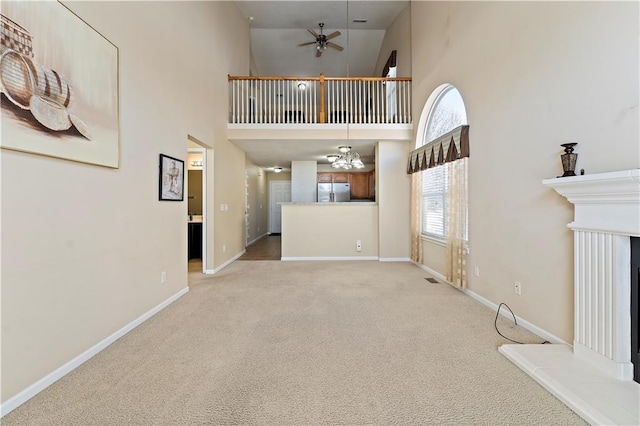 unfurnished living room featuring high vaulted ceiling, light colored carpet, and ceiling fan with notable chandelier