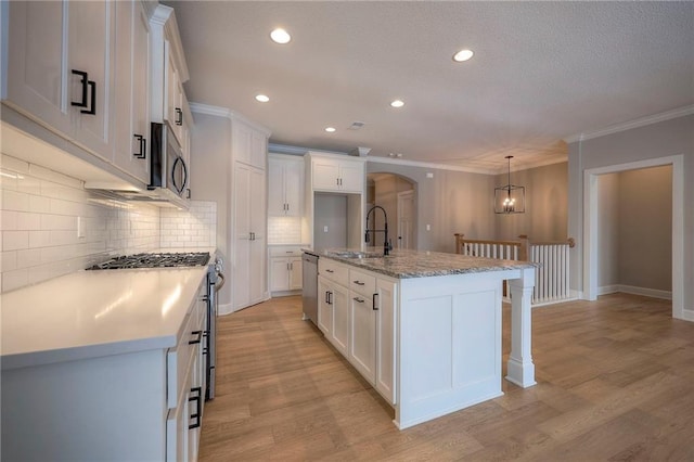 kitchen with white cabinets, decorative light fixtures, a kitchen island with sink, and appliances with stainless steel finishes