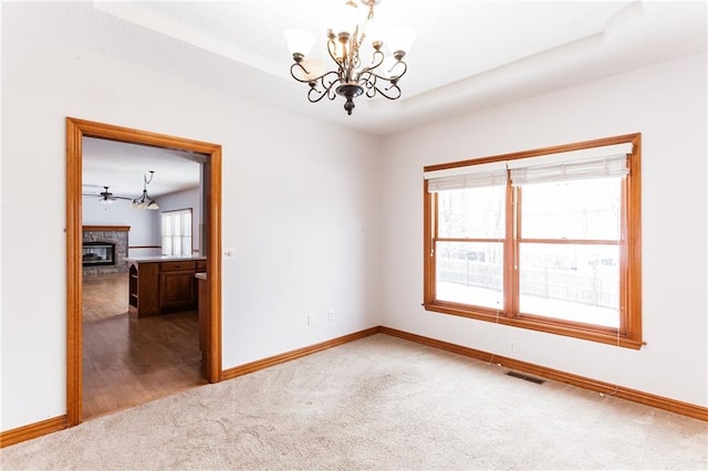 carpeted empty room featuring baseboards, a glass covered fireplace, visible vents, and an inviting chandelier