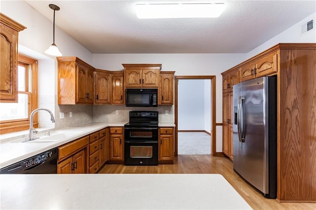 kitchen featuring a sink, visible vents, light countertops, black appliances, and light wood finished floors