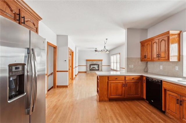 kitchen with a peninsula, a fireplace, stainless steel fridge with ice dispenser, dishwasher, and light wood finished floors