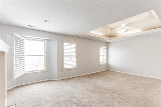 unfurnished room featuring a textured ceiling, visible vents, a ceiling fan, a tray ceiling, and carpet