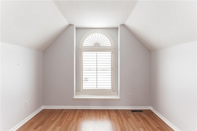 bonus room with light wood-type flooring, visible vents, vaulted ceiling, and a textured ceiling