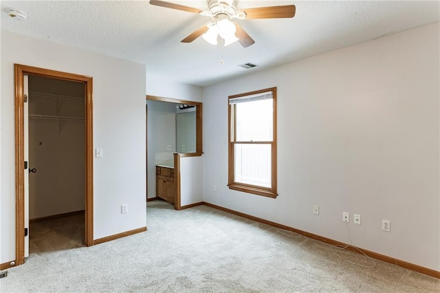 unfurnished bedroom with baseboards, visible vents, light colored carpet, a spacious closet, and a textured ceiling