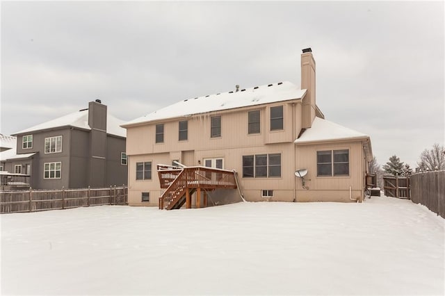 snow covered back of property featuring a deck, a fenced backyard, a chimney, and stairs