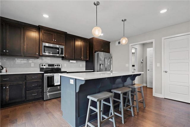 kitchen featuring dark wood-style floors, decorative light fixtures, a center island with sink, stainless steel appliances, and light countertops