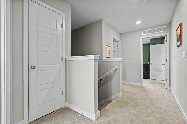 hall with light colored carpet, baseboards, visible vents, and an upstairs landing