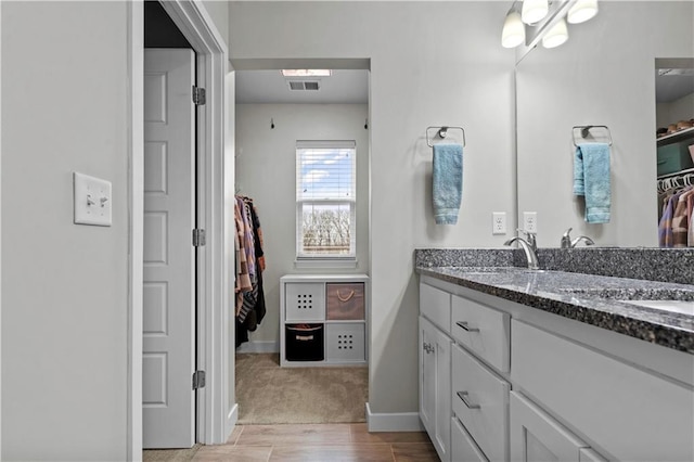 bathroom featuring a sink, visible vents, baseboards, a spacious closet, and double vanity