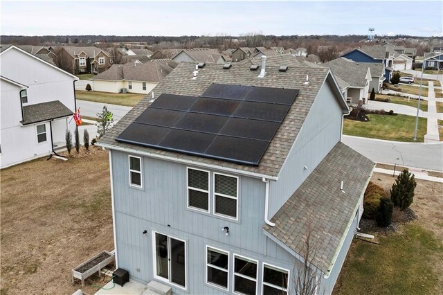 back of property featuring a shingled roof, roof mounted solar panels, and a residential view