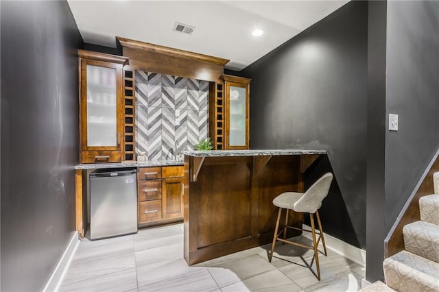 bar with fridge and light stone countertops