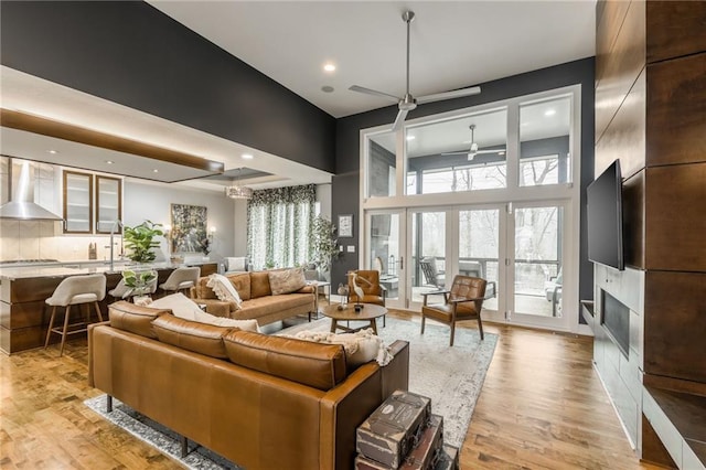 living room featuring light hardwood / wood-style flooring, french doors, ceiling fan, and a high ceiling