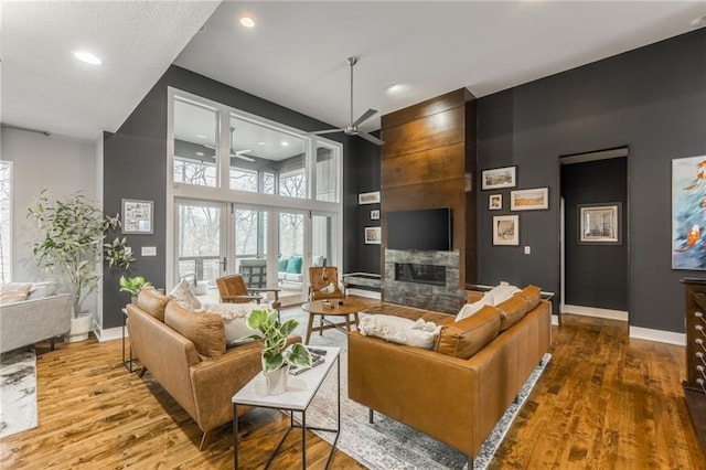 living room featuring a high ceiling, wood-type flooring, a large fireplace, and ceiling fan